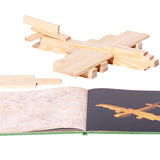 Wooden aeroplane model on a white background next to the Kapla simple architecture art book on a white background