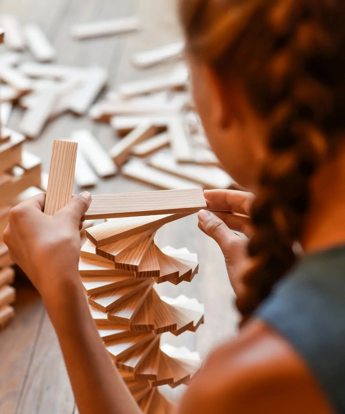 Child building a spiral tower made from the natural Kapla wooden construction planks 