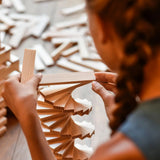 Child building a spiral tower made from the natural Kapla wooden construction planks 