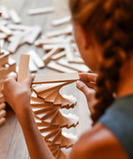 Child building a spiral tower made from the natural Kapla wooden construction planks 
