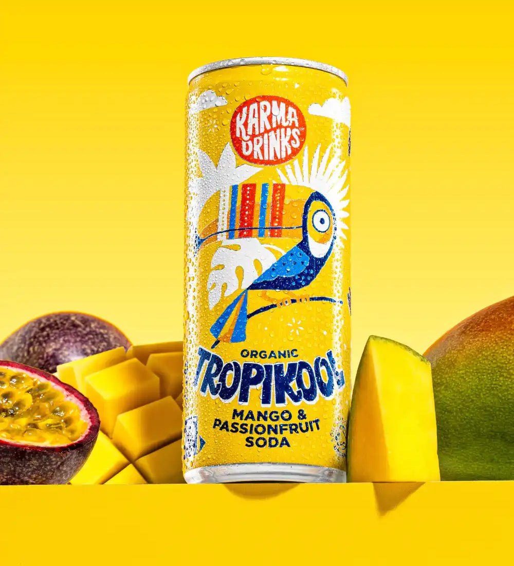 Karma organic tropikool mango & passion fruit soda in yellow coloured illustrated can surrounded by cut passion fruit and mango.
