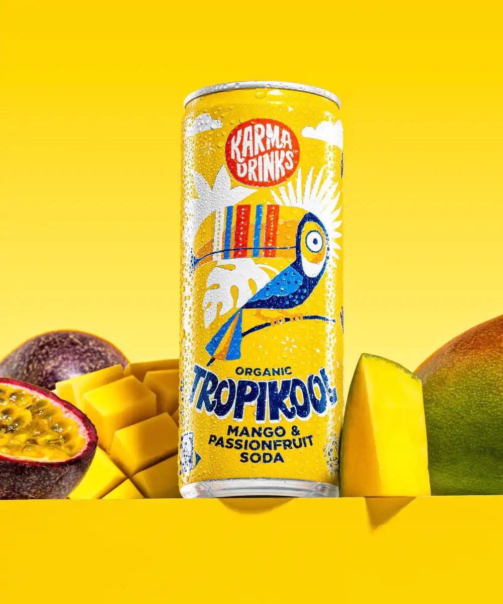 Karma organic tropikool mango & passion fruit soda in yellow coloured illustrated can surrounded by cut passion fruit and mango.