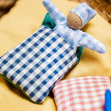 A blue waldorf kathe kruse doll inside a blue gingham blanket sitting inside a wicker basket