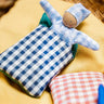 A blue waldorf kathe kruse doll inside a blue gingham blanket sitting inside a wicker basket