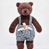 Käthe Kruse Bella brown bear soft toy wearing blue and white gingham dungarees with white waldorf doll in pocket