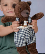 Käthe Kruse Bella brown bear soft toy wearing blue and white gingham dungarees with a small doll in it's front pocket.