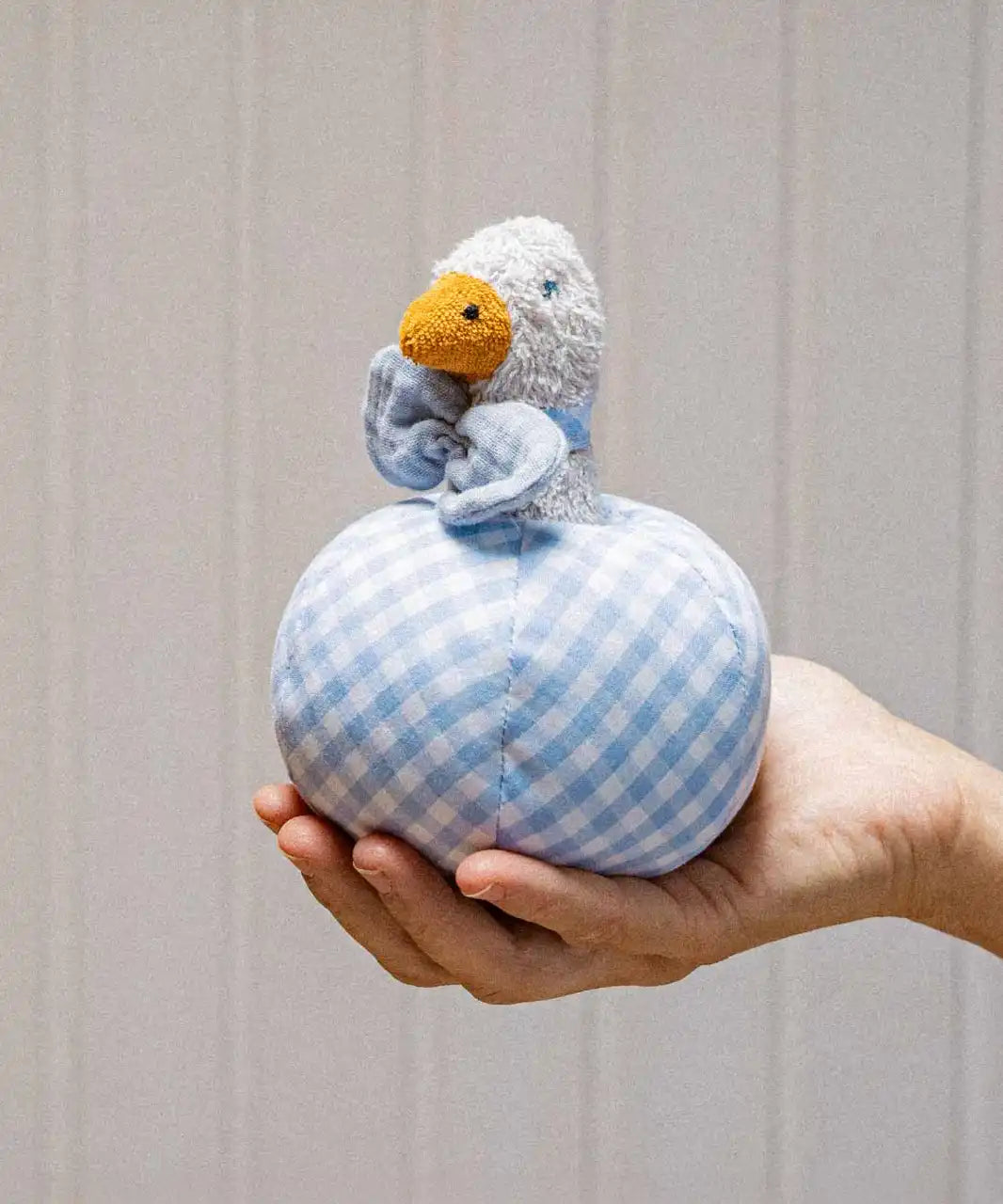 Käthe Kruse Ebba duck soft toy rattle and ball. Small duck wearing a blue and white check bowtie that is placed inside a slot in a matching ball. 