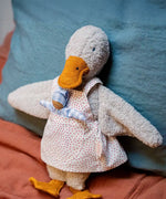 Käthe Kruse Eva duck standing soft toy wearing a white apron with red dots all over. There is a small doll in the apron pocket.