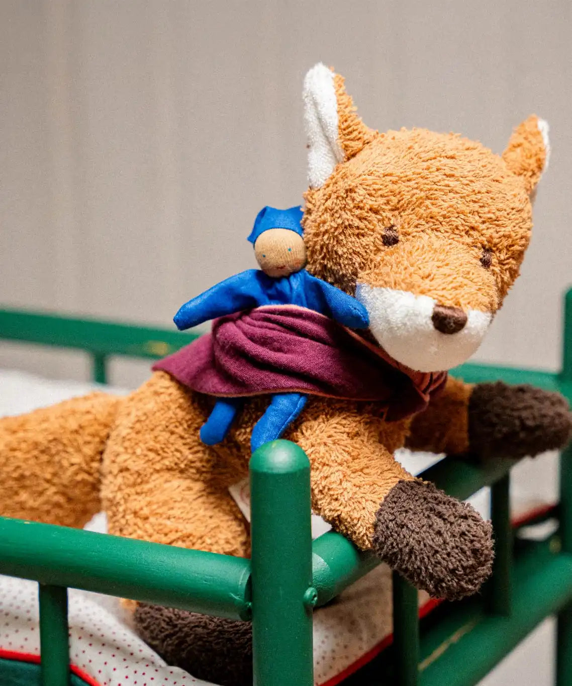 Käthe Kruse Finn fox lying soft toy placed in a green dolls cot. 