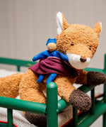 Käthe Kruse Finn fox lying soft toy placed in a green dolls cot. 
