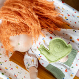 Käthe Kruse Waldorf doll Elsa laying in a dolls cot with the green felt snail that comes with her placed on her.