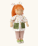 Käthe Kruse Waldorf doll Elsa with long red wavy hair and fair skin. White patterned tunic top with pink linen style trousers underneath. White patterned bow in her hair with green and white sneaker style shoes.
