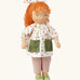 Käthe Kruse Waldorf doll Elsa with long red wavy hair and fair skin. White patterned tunic top with pink linen style trousers underneath. White patterned bow in her hair with green and white sneaker style shoes.