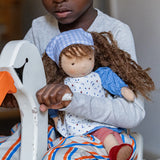 Child holding a Käthe Kruse Waldorf doll Tilda in their arms while riding a rocking swan toy.