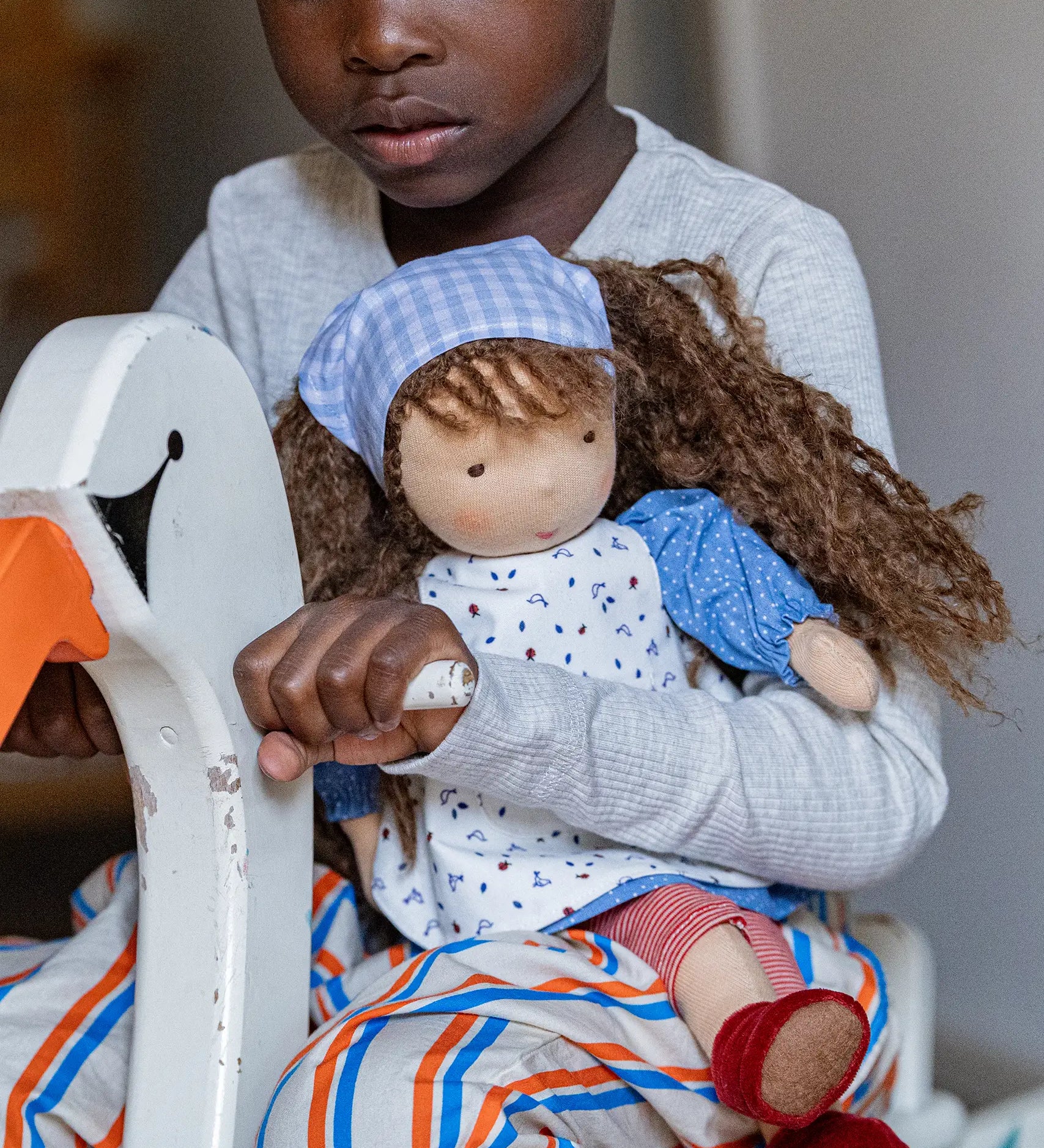 Child holding a Käthe Kruse Waldorf doll Tilda in their arms while riding a rocking swan toy.