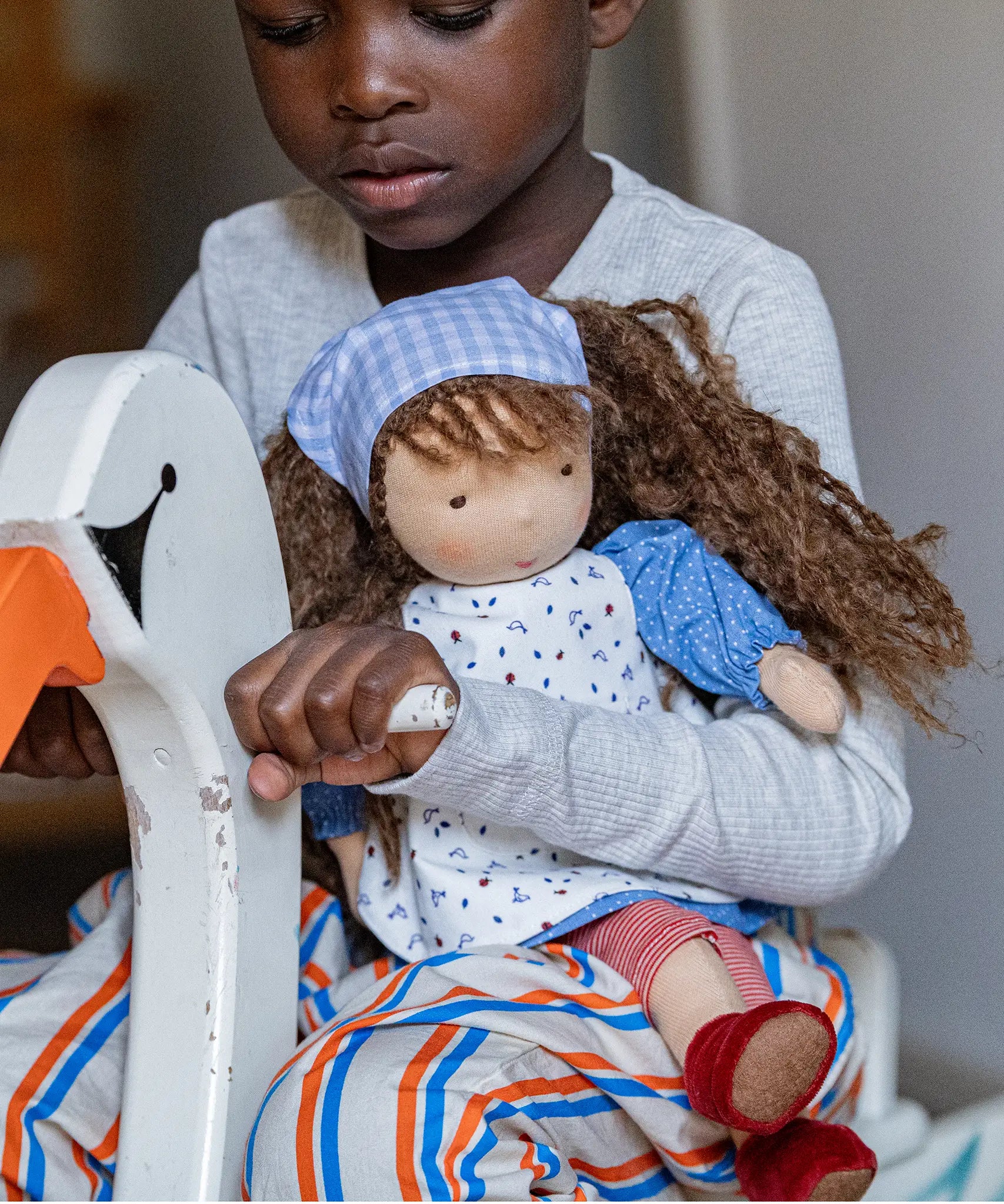Child holding a Käthe Kruse Waldorf doll Tilda in their arms while riding a rocking swan toy.