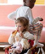 Child holding a Hannah Kathe Kruse waldorf doll and sitting in a trailer on a bike