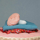 Kathe Kruse mushroom soft grabber toy lying on top of a sheets in a wicker basket. Showing a red gingham top and white stem