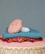 Kathe Kruse mushroom soft grabber toy lying on top of a sheets in a wicker basket. Showing a red gingham top and white stem