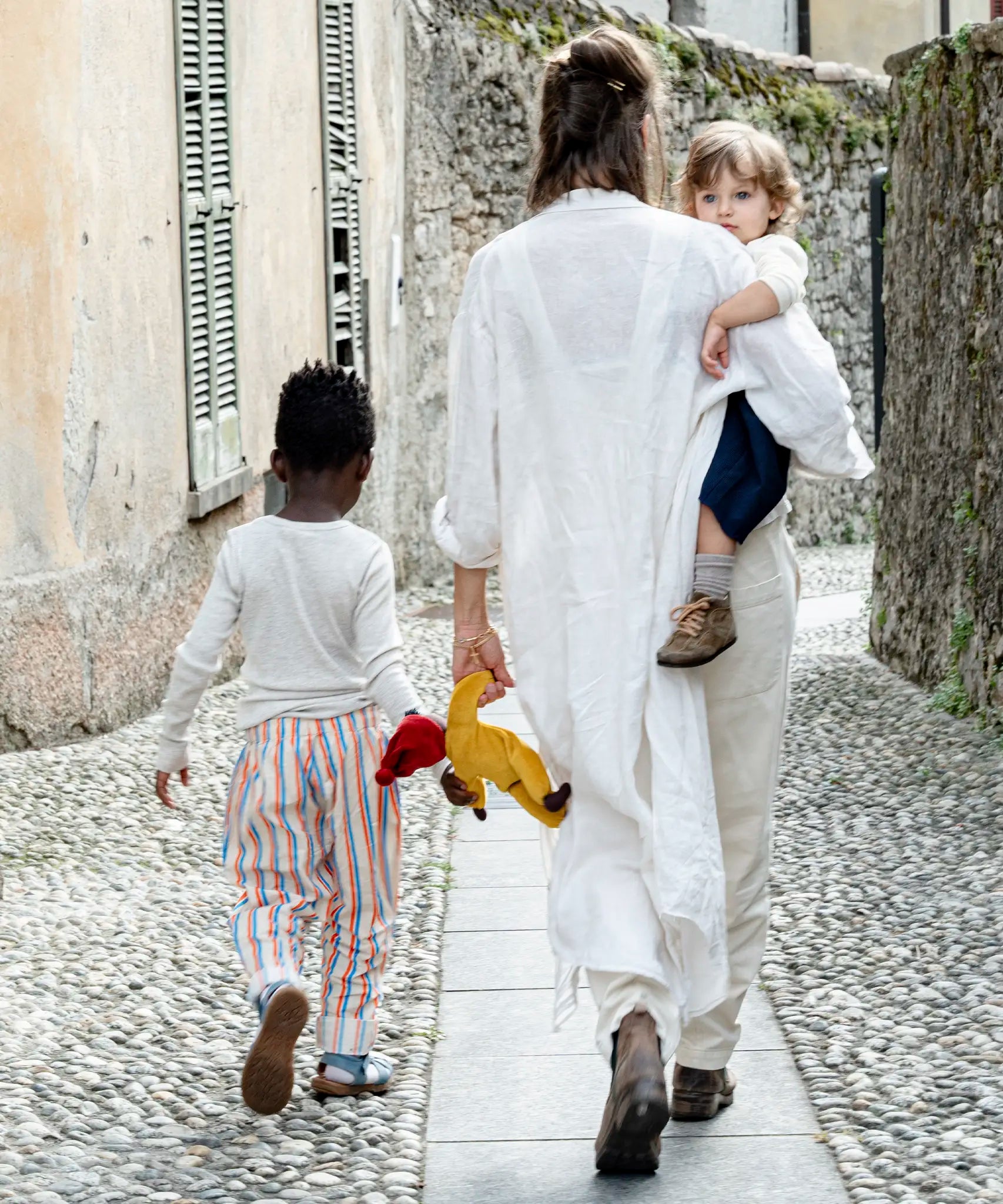 Mother carrying child with a saffron Kathe Kruse doll in hand and a child holding the doll