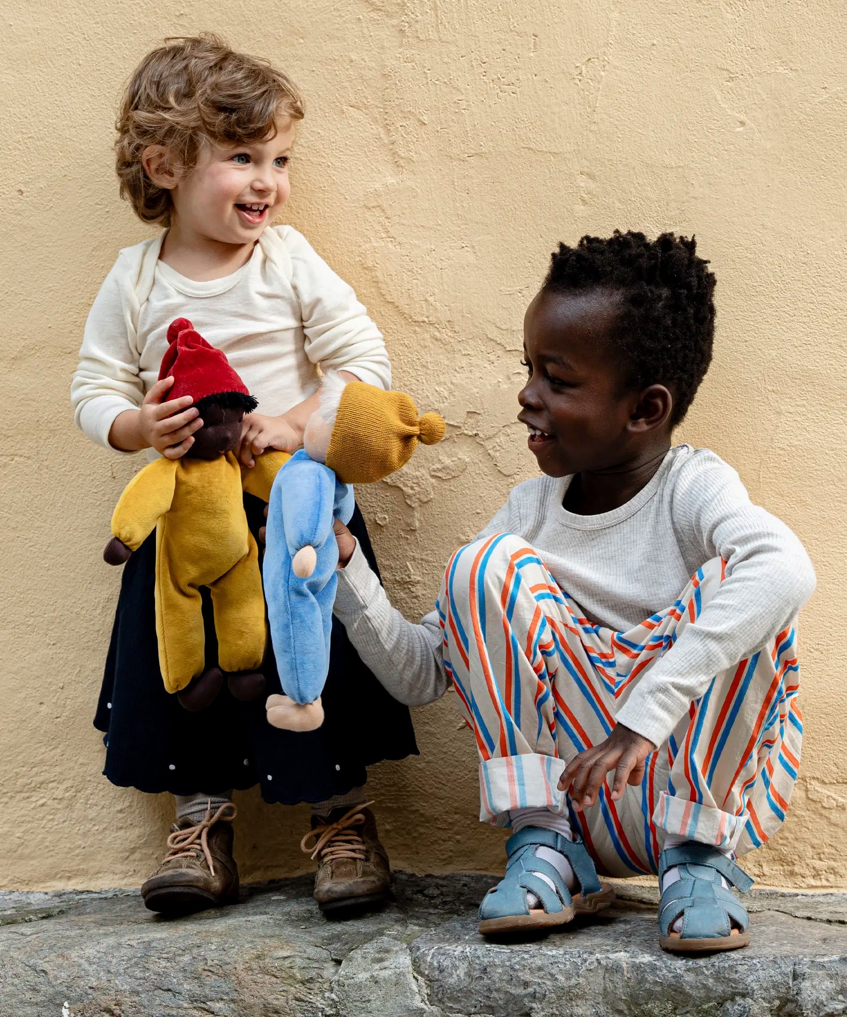 Child playing with Kathe Kruse Saffron nana waldorf doll with another child holding a cloud waldorf doll