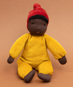 Kathe Kruse Saffron nana waldorf doll sitting against a burnt orange background.