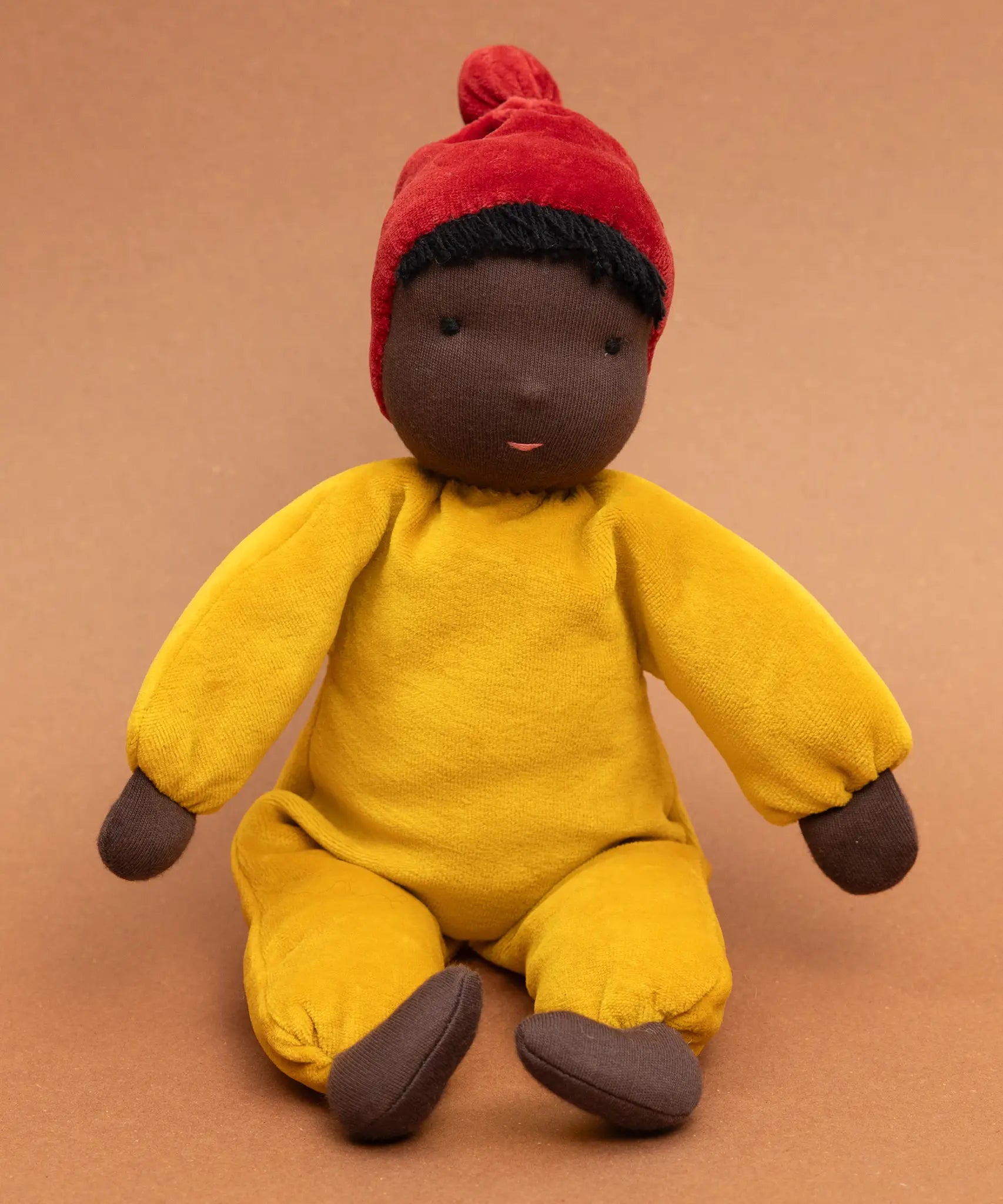 Kathe Kruse Saffron nana waldorf doll sitting against a burnt orange background.