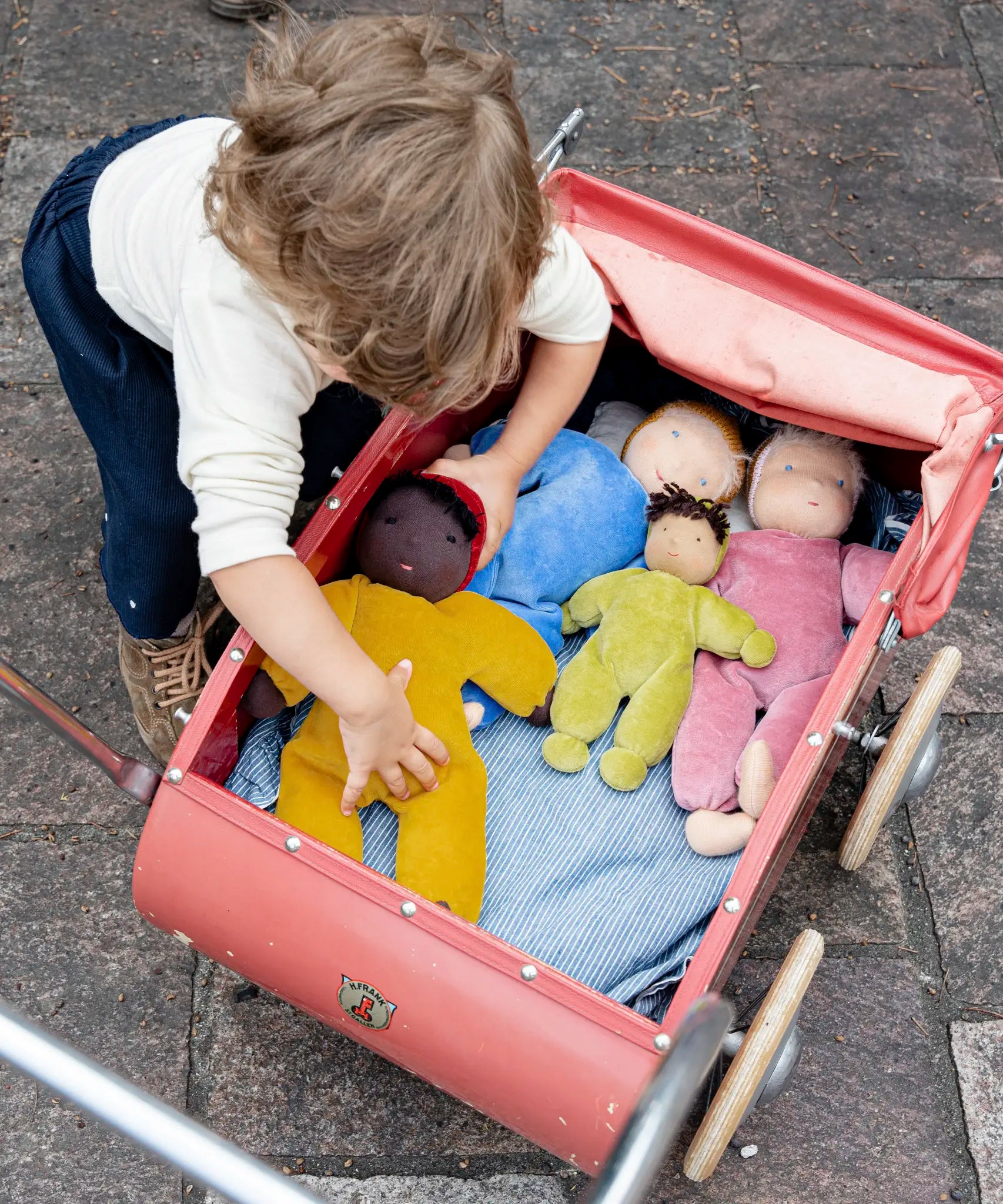 Child playing with Kathe Kruse nana Saffron waldorf doll with other waldorf dolls in a pram