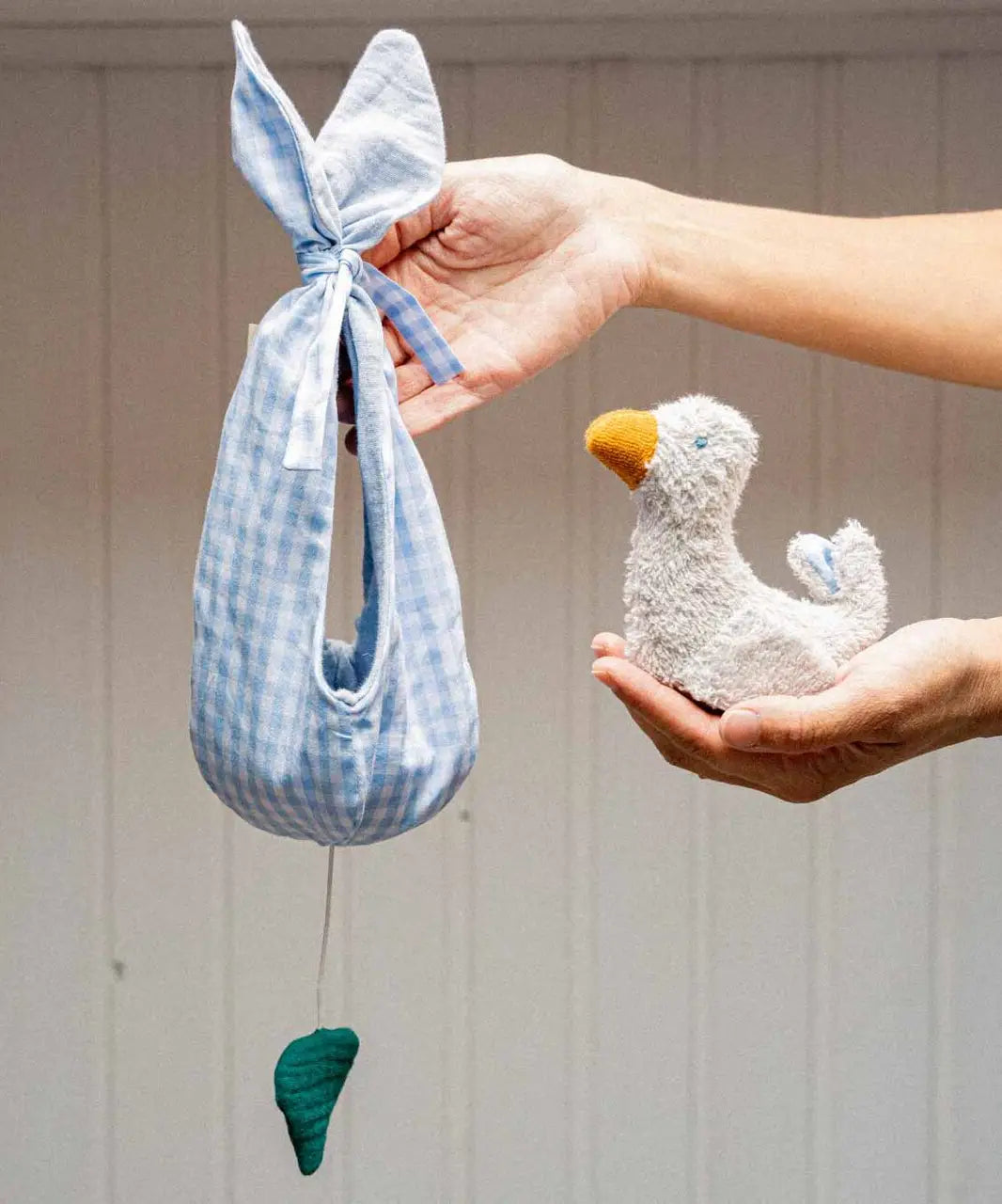 Adult hand holding a white soft duckling toy and a blue gingham fabric nest 
