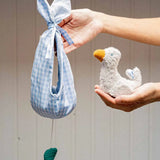 Adult hand holding a white soft duckling toy and a blue gingham fabric nest 