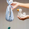 Adult hand holding a white soft duckling toy and a blue gingham fabric nest 