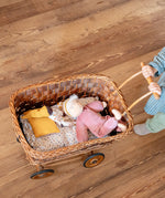 Käthe Kruse Waldorf Doll Nini Sunshine. and large Waldorf doll placed in a wicker dolls pram pushed by a child.