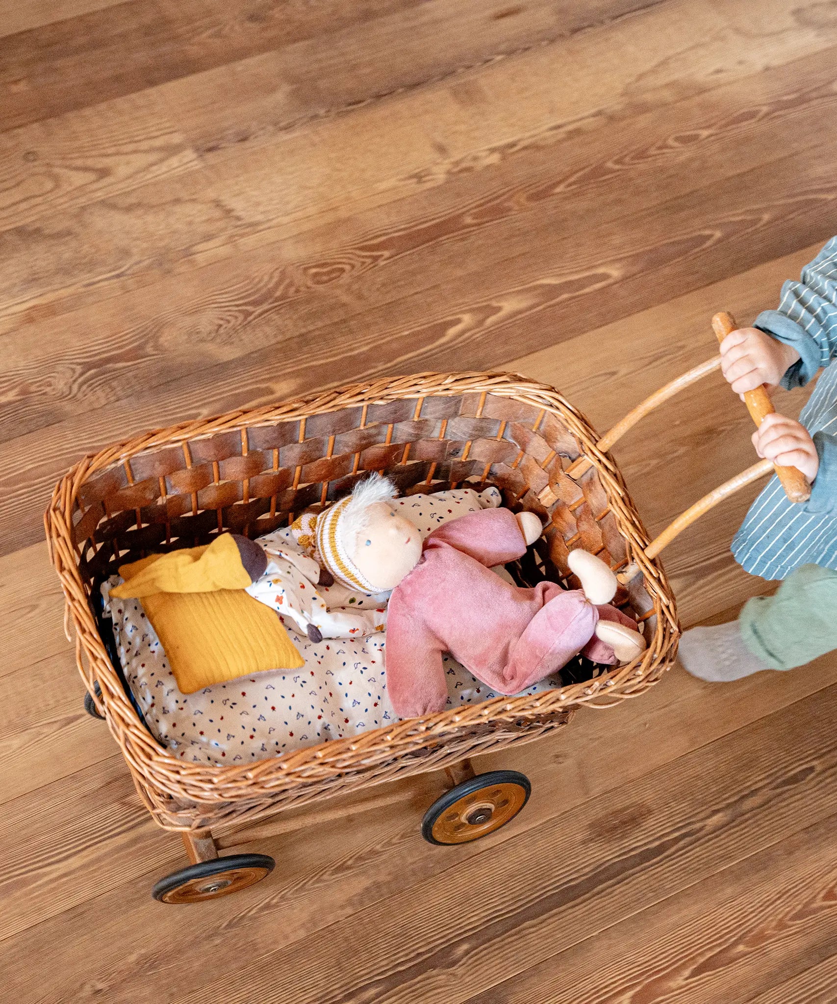 Käthe Kruse Waldorf Doll Nini Sunshine. and large Waldorf doll placed in a wicker dolls pram pushed by a child.
