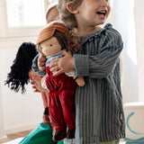 Smiling child holding Kathe Kruse Toni Waldorf Doll; a handmade doll with an organic cotton overall outfit and organic wool hair. 