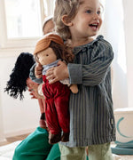 Smiling child holding Kathe Kruse Toni Waldorf Doll; a handmade doll with an organic cotton overall outfit and organic wool hair. 