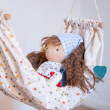 Käthe Kruse Waldorf doll Tilda with long brown hair and fair skin placed in a white patterned hammock. 