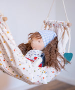 Käthe Kruse Waldorf doll Tilda with long brown hair and fair skin placed in a white patterned hammock. 