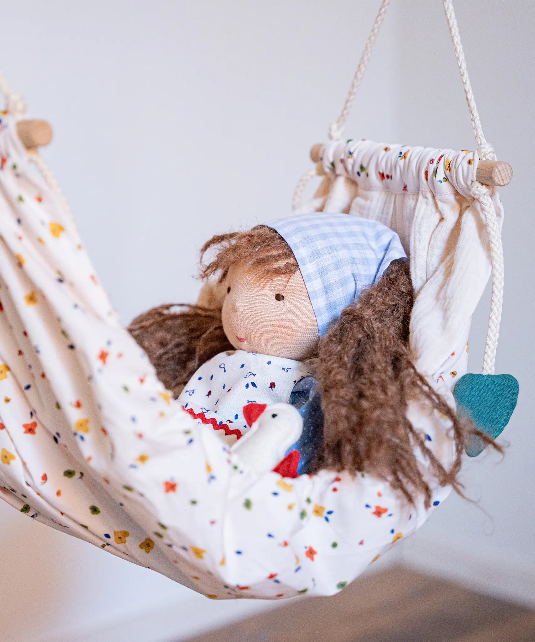 Käthe Kruse Waldorf doll Tilda with long brown hair and fair skin placed in a white patterned hammock. 