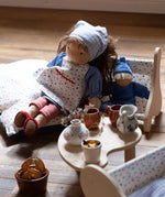 Käthe Kruse Waldorf doll Tilda placed in a wooden seat next to a smaller blue doll. 