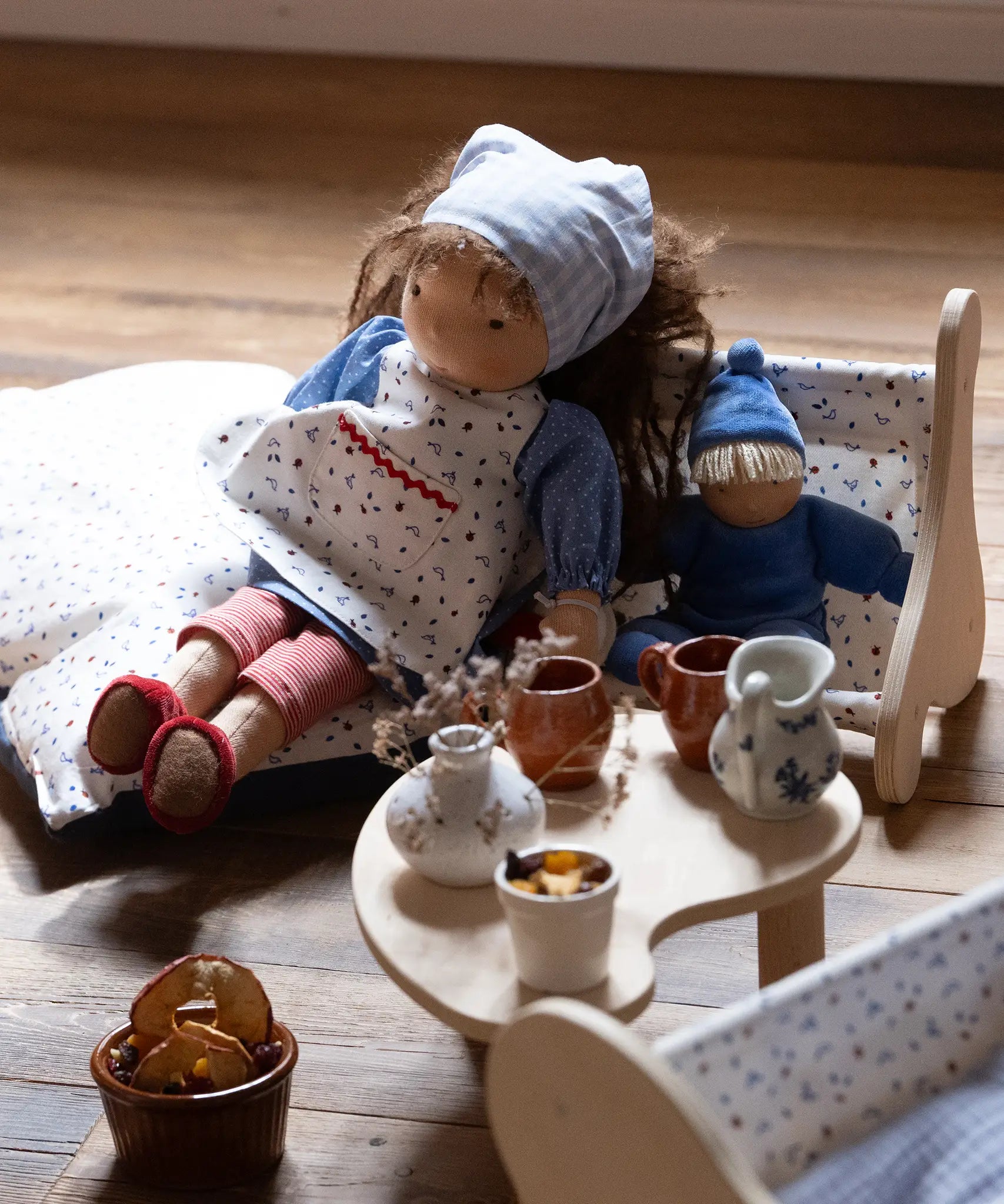 Käthe Kruse Waldorf doll Tilda placed in a wooden seat next to a smaller blue doll. 