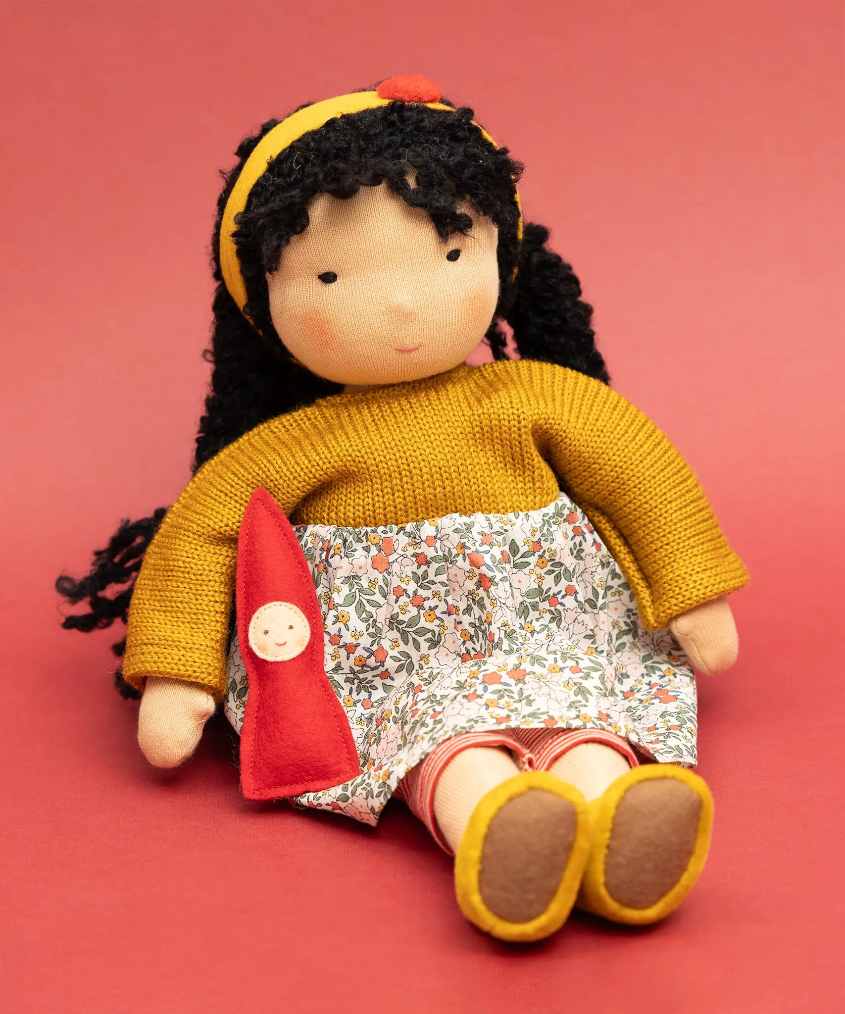 Käthe Kruse Waldorf Doll Kiki in a seated position with the ref felt gnome placed in the crook of her arm.