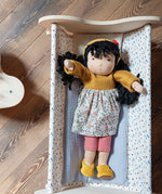Käthe Kruse Waldorf Doll Kiki placed in a wooden doll's cot.