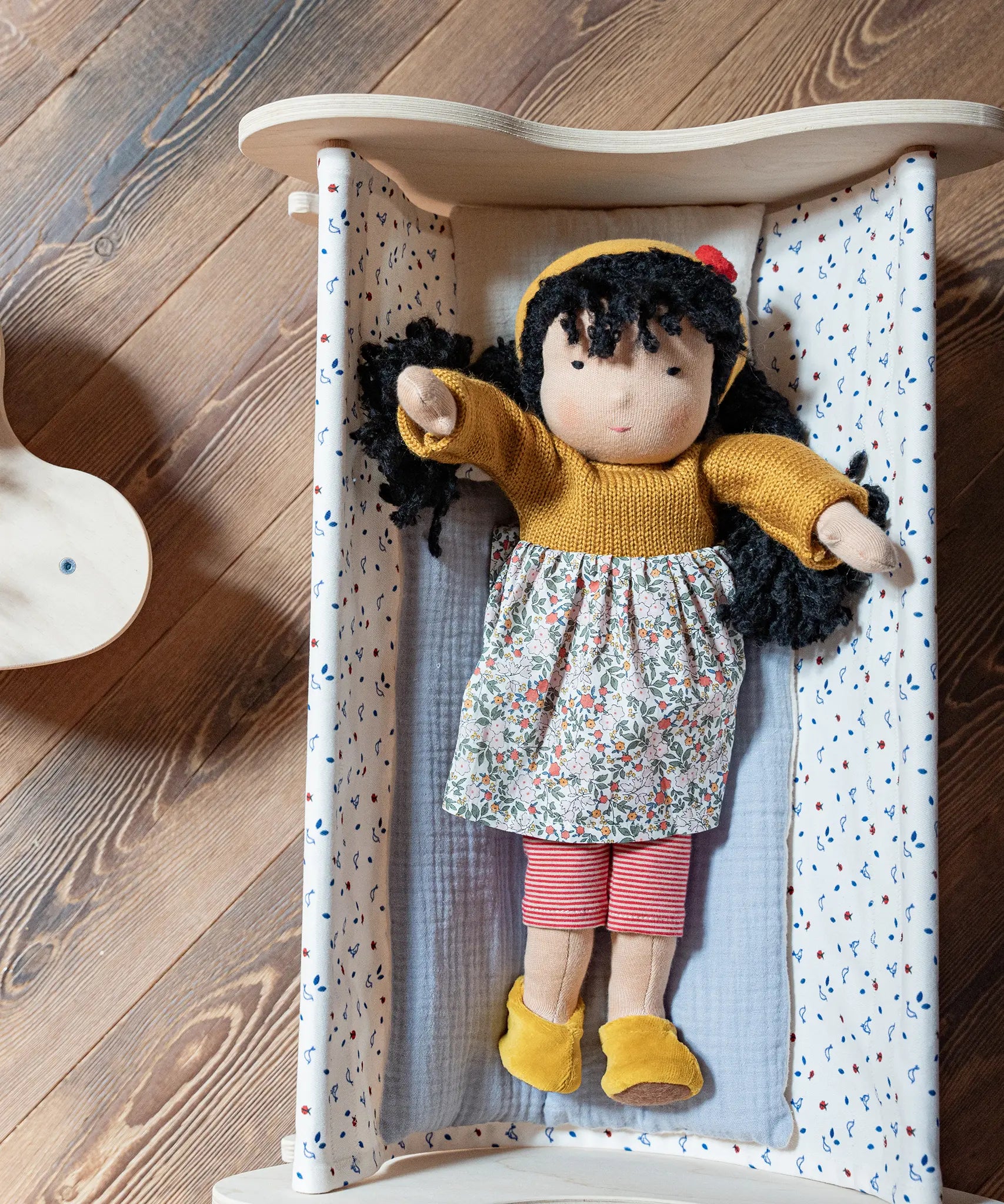 Käthe Kruse Waldorf Doll Kiki placed in a wooden doll's cot.