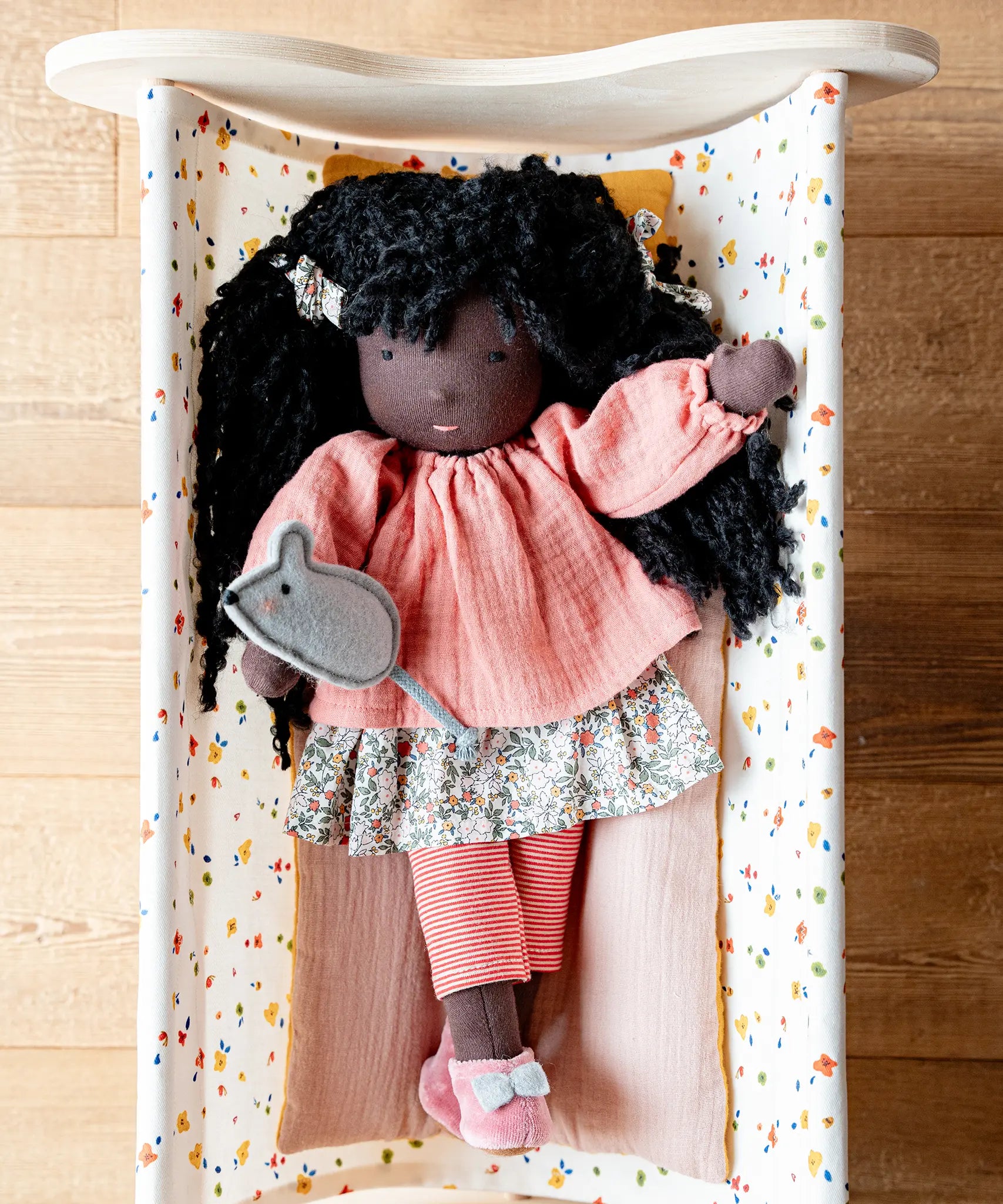 Käthe Kruse Waldorf Doll Nia placed in a doll's crib with the felt mouse on her hand.