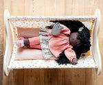 Käthe Kruse Waldorf Doll Nia in a doll's crib with a grey felt mouse on her hand.