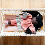 Käthe Kruse Waldorf Doll Nia in a doll's crib with a grey felt mouse on her hand.