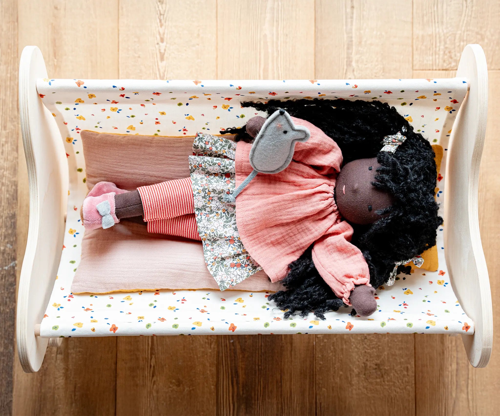 Käthe Kruse Waldorf Doll Nia in a doll's crib with a grey felt mouse on her hand.