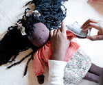 Käthe Kruse Waldorf Doll Nia placed in a laying position with a child placing the grey mouse on her hand. 
