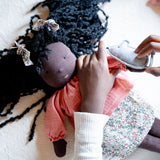 Käthe Kruse Waldorf Doll Nia placed in a laying position with a child placing the grey mouse on her hand. 