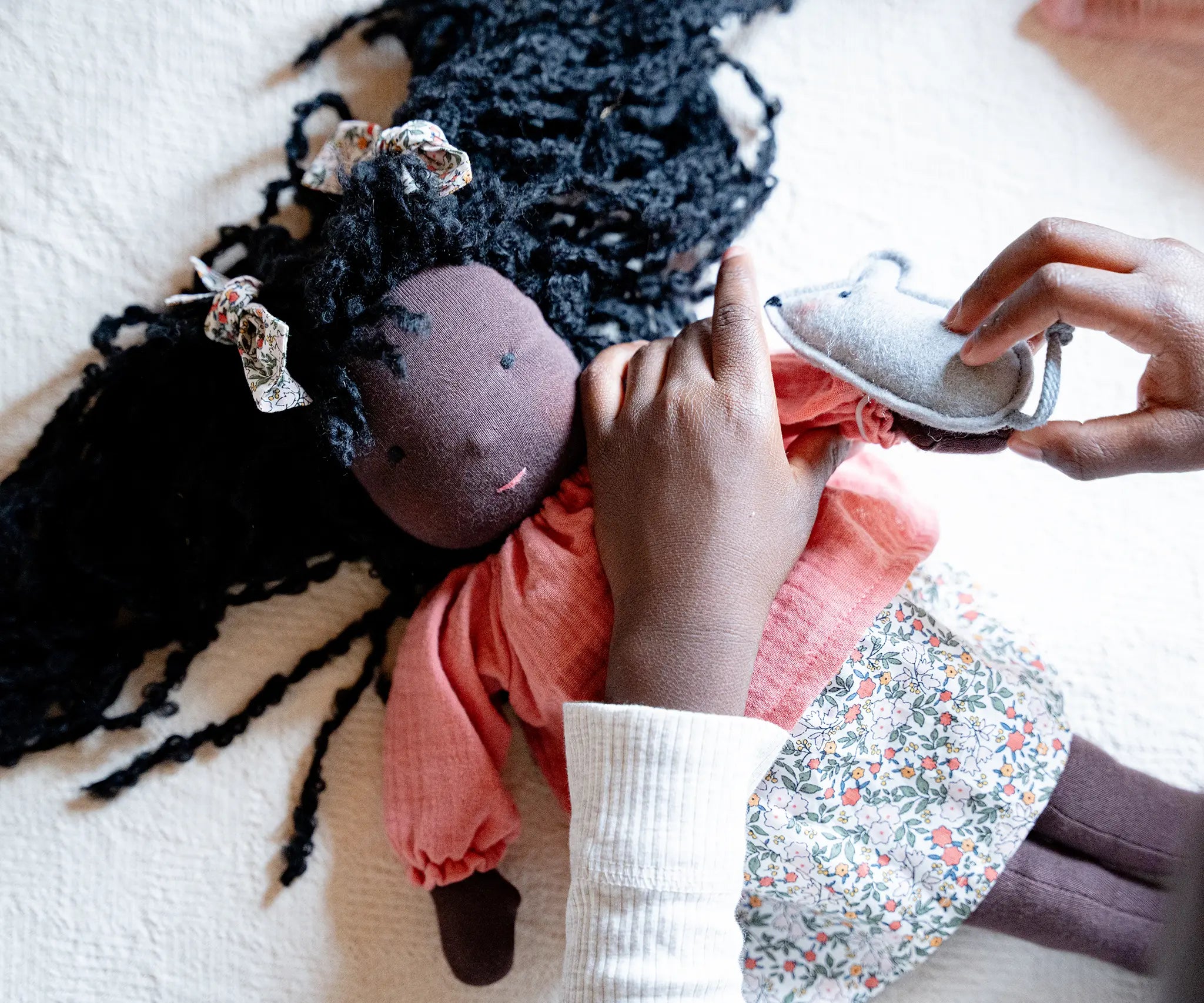Käthe Kruse Waldorf Doll Nia placed in a laying position with a child placing the grey mouse on her hand. 